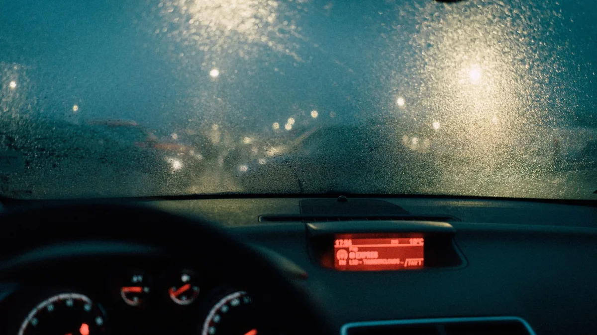 Rain streaming down a windshield with blurred taillights ahead on the highway