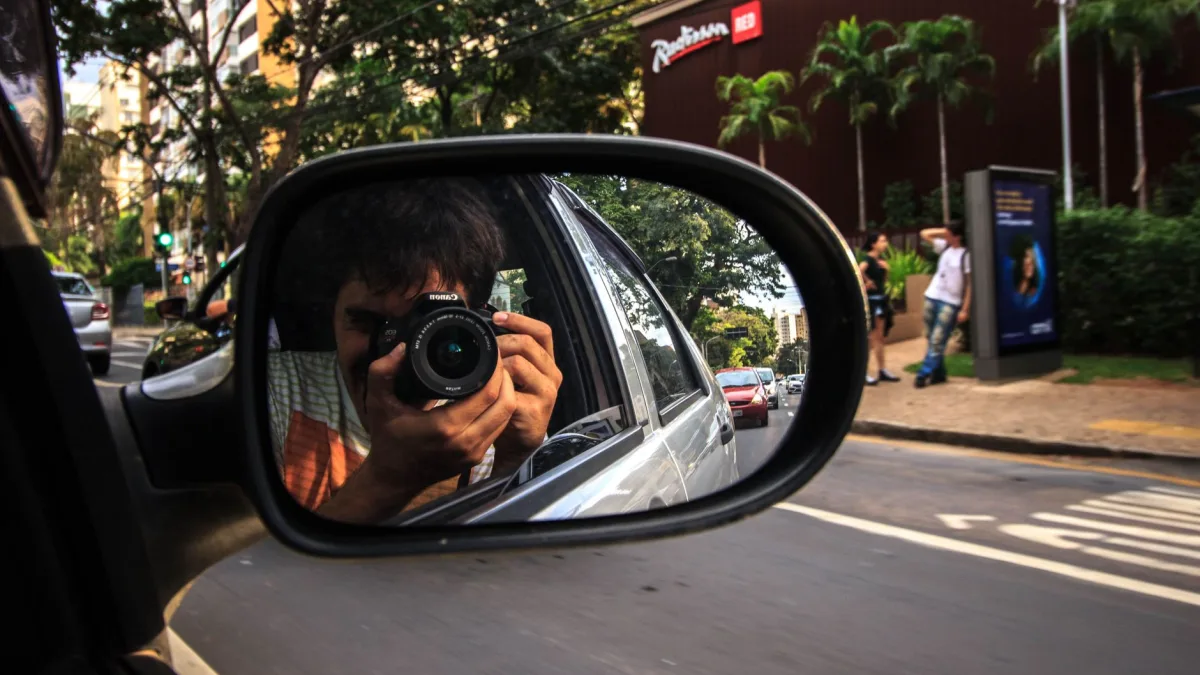 Wide-angle camera lens under a car side mirror covered in road spray
