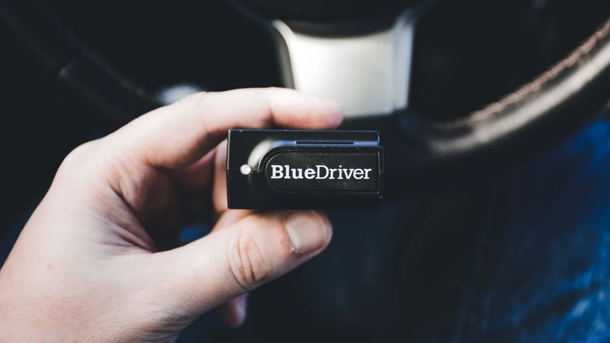 Bluetooth diagnostic dongle plugged into a vehicle OBD2 port under the dash