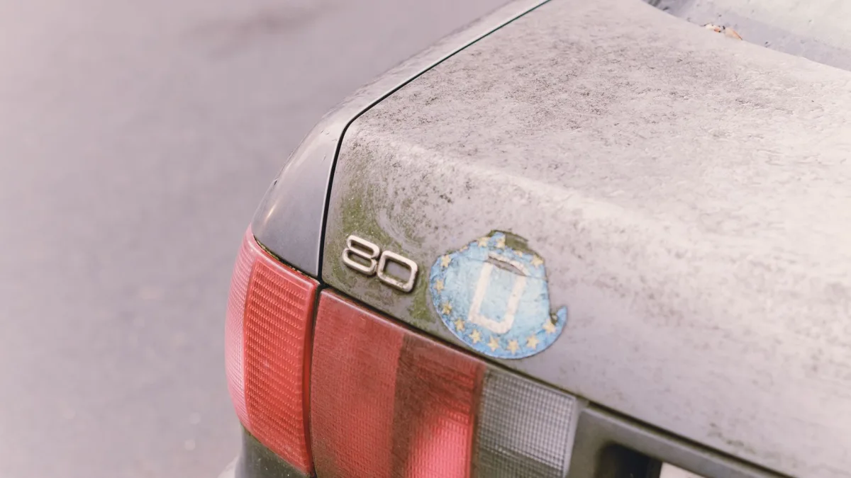 Road salt and grime caked over a rear bumper corner near a blind spot sensor