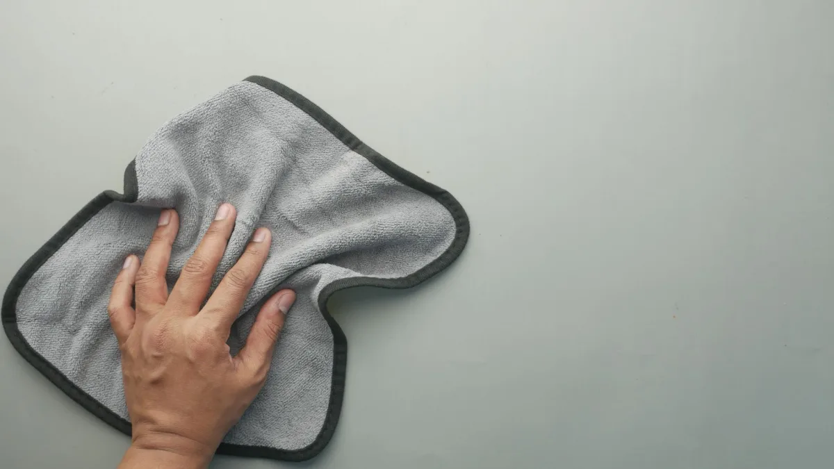 A hand wiping the rear bumper corner clean over a hidden blind spot sensor