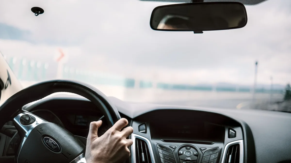Driver keeping hands on the wheel while the car holds the center of a highway lane