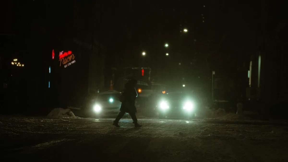 A person stepping into a crosswalk in front of an approaching vehicle at dusk
