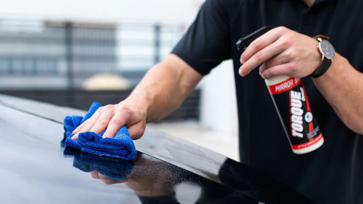 Gloved hand spraying cleaner near a rear bumper camera housing