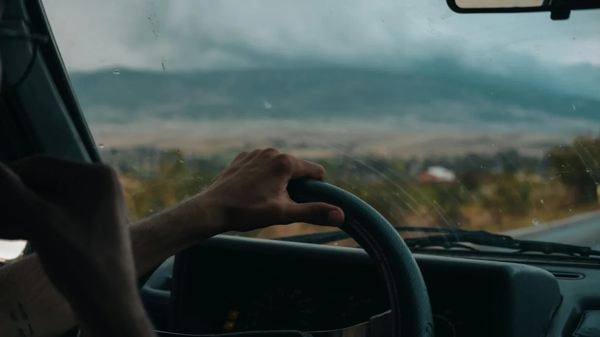 Two hands resting with light grip on a steering wheel during highway driving